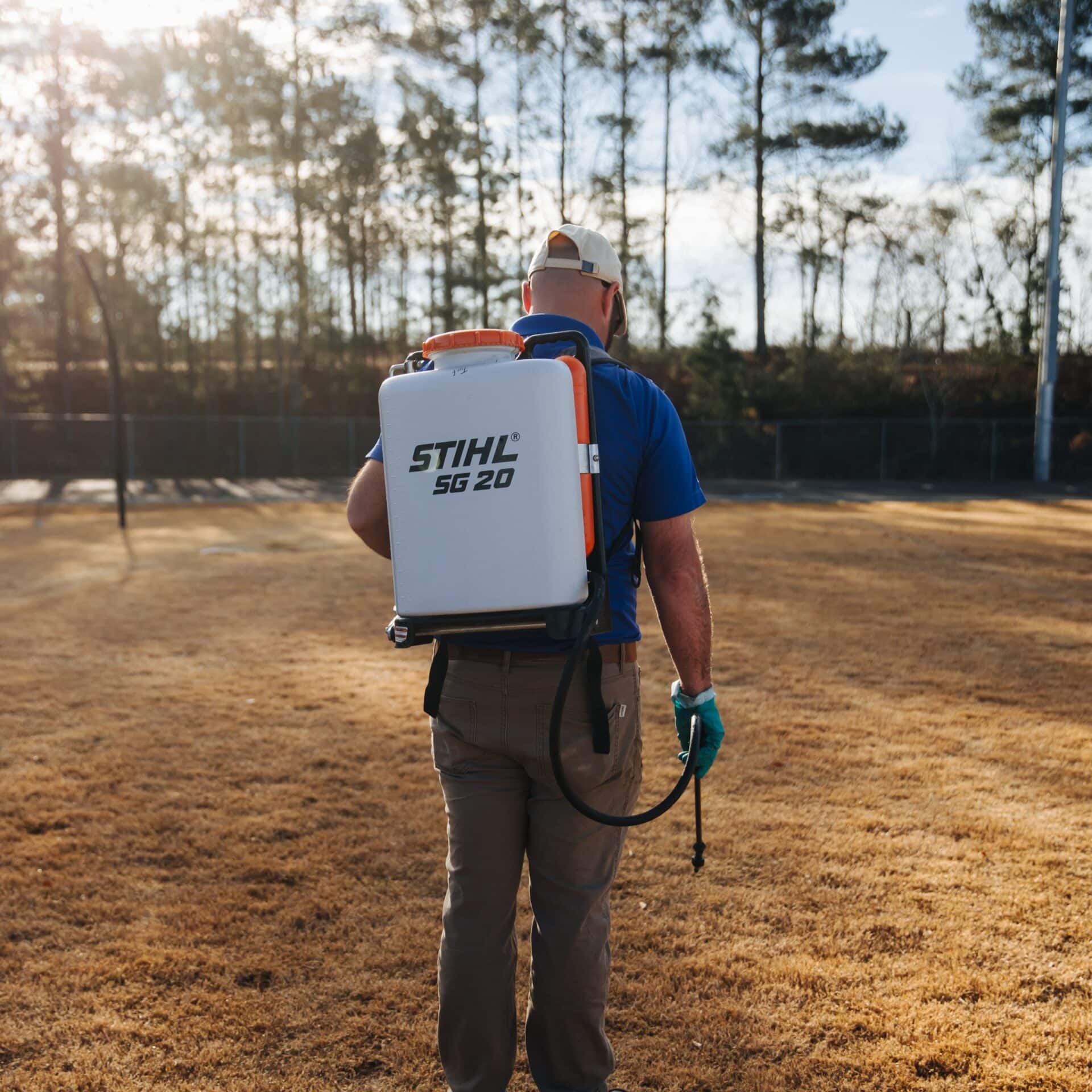 man spraying an open field with trees in the background